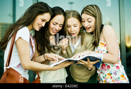 Four young female friends looking and laughing at notebook Stock Photo