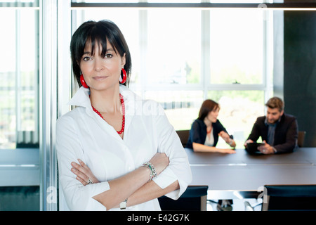 Businesswoman at entrance of meeting room, couple in background Stock Photo