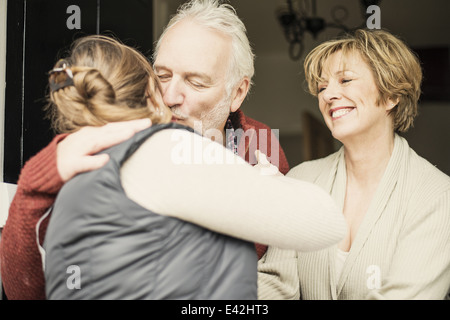 Father kissing adult daughter, mother smiling Stock Photo