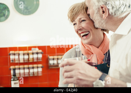 Senior man kissing woman in kitchen, woman laughing Stock Photo