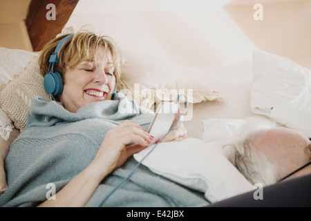Mature woman lying on bed using mp3 player Stock Photo