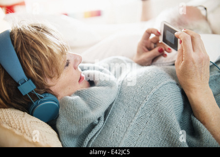 Mature woman lying on bed using mp3 player