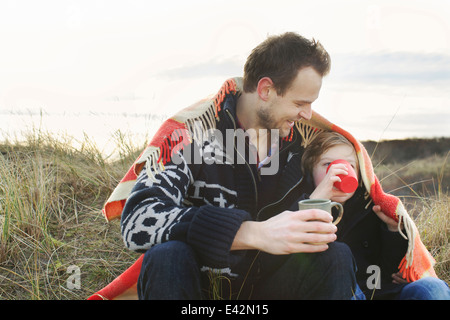 Smiling mid adult man and son wrapped in blanket on sand dunes