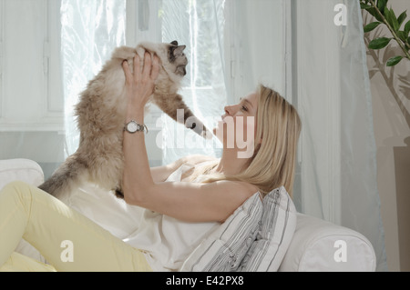 Young woman on sofa holding up cat Stock Photo