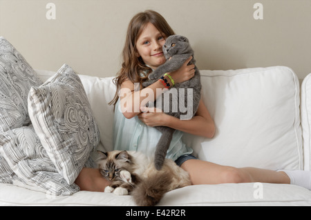 Girl with two cats on sitting room sofa Stock Photo