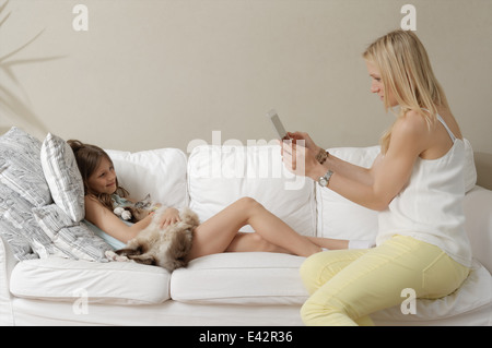 Mother photographing daughter and cat on sofa Stock Photo