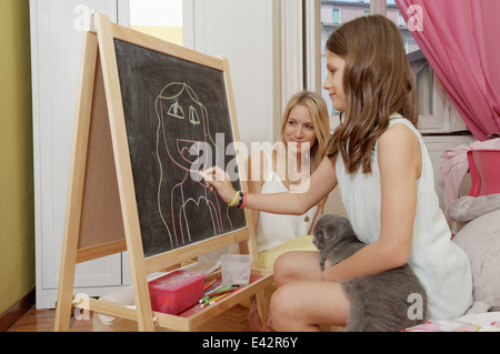 Girl drawing portrait of her mother on blackboard Stock Photo