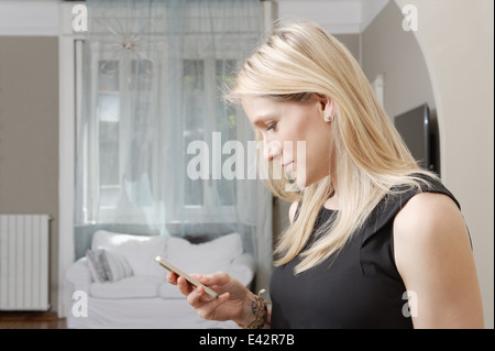 Young woman reading text message on smartphone in dining room Stock Photo