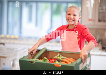 Teenage girl carrying vegetable box in kitchen Stock Photo