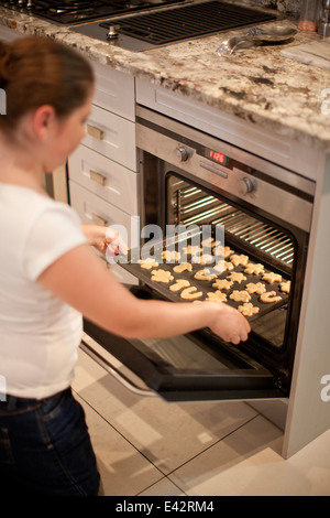 Teenage girl placing baking tray of biscuits in oven Stock Photo