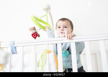 Alert baby boy gazing out from crib Stock Photo