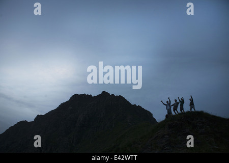 Silhouette of four young adult men with arms raised on top of mountain Stock Photo