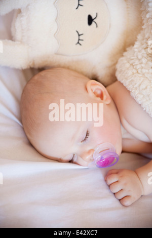 Baby girl sleeping in crib with cuddly toy Stock Photo