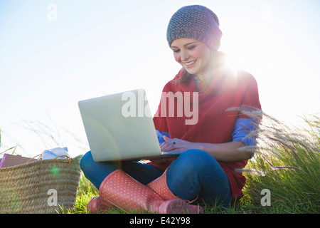Young woman using laptop whilst sitting in long grass Stock Photo