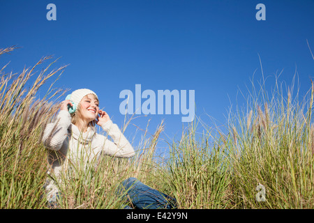 Young woman sitting in long grass listening to headphones Stock Photo