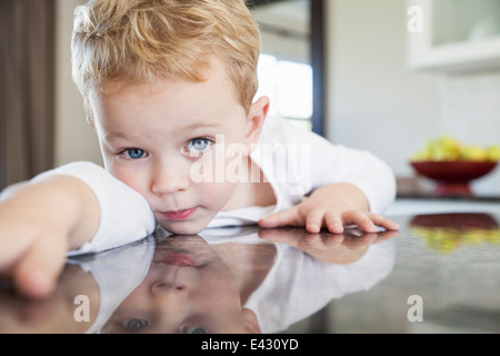 Portrait of three year old boy leaning forward on kitchen bench Stock Photo
