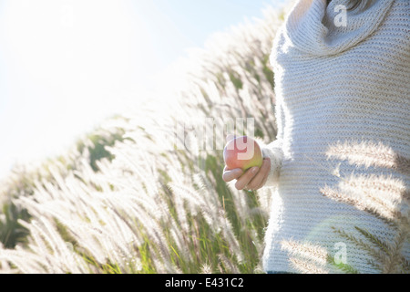 Cropped shot of young woman holding an apple in long grass Stock Photo