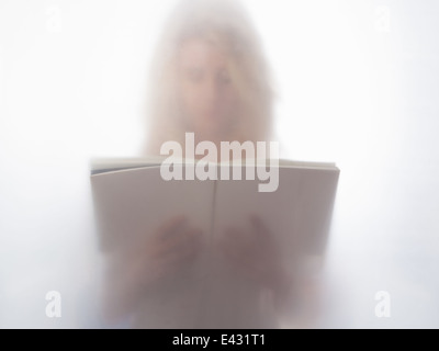 Young woman reading book behind frosted glass Stock Photo