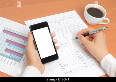 Businesswoman works at her workplace with smartphone, graphs and tables Stock Photo