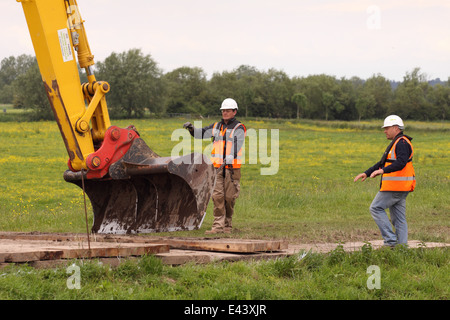 Environment Agency staff contractors working with an excavator digger wearing hard hats and high viz jackets Stock Photo