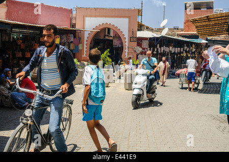 Riding scooters and bicycles past the entrance to the souq, Marrakech, Morocco. Stock Photo
