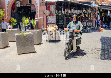 Riding scooters and bicycles past the entrance to the souq, Marrakech, Morocco. Stock Photo