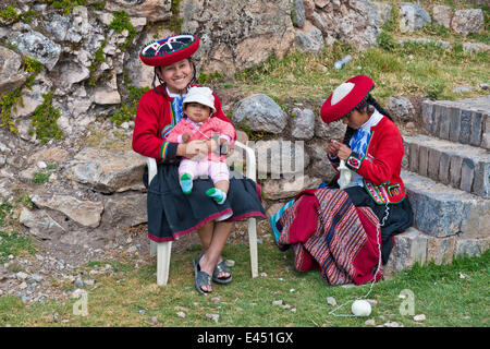 Two women, Quechua Indians, in traditional dress, one smiling woman sitting on a chair holding a toddler, another woman sitting Stock Photo