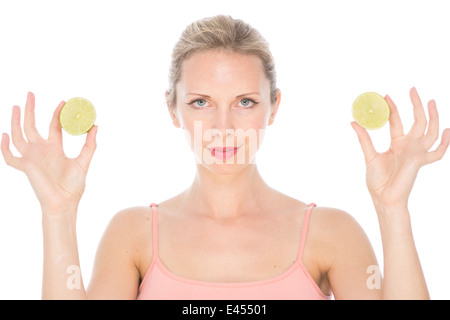 attractive young blonde woman in pink vest top holds up slices of lime lemon to her eyes smiling Stock Photo