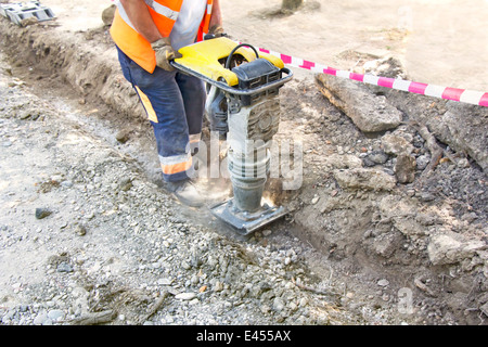 Worker uses compactor to firm soil at worksite Stock Photo