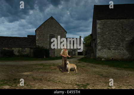 Portrait of mature traditional farmer and his lurcher dog in farmyard Stock Photo