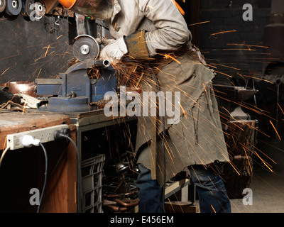 Blacksmith grinding metal on a machine in workshop Stock Photo