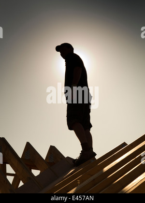 self building house, constructing roof, roofer on top of roof silhouetted against sun Stock Photo