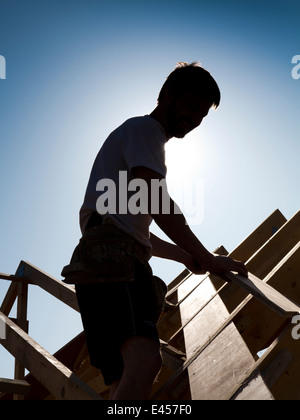 self building house, constructing roof, roofer positioning roof trussed silhouetted against sun Stock Photo