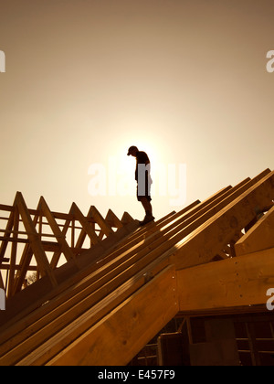 self building house, constructing roof, roofer on top of roof silhouetted against sun Stock Photo