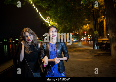 Two female friends strolling along riverside at night Stock Photo