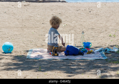 Little boy with curly blond hair playing in the sand in the shade on the beach at Cherry Beach in Toronto Ontario Canada Stock Photo