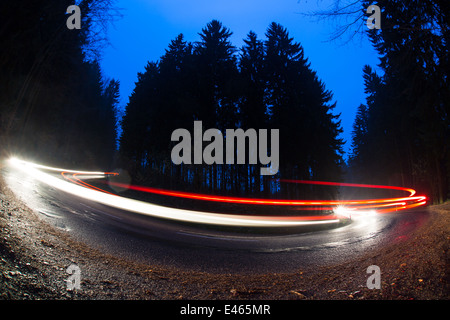 Cars going fast through a curve on a forest road at dusk, on a rainy day - i.e. Potentially dangerous driving conditions Stock Photo