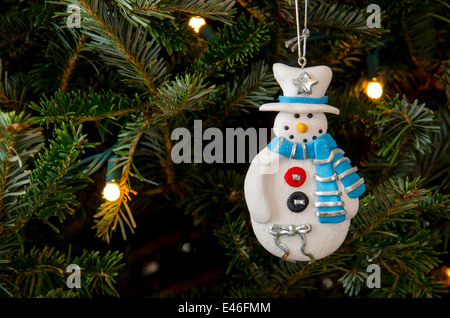 A clay Christmas ornament in the shape of a snowman wears a white hat and blue and silver scarf Stock Photo