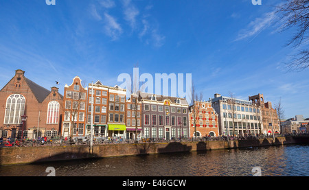 AMSTERDAM, NETHERLANDS - MARCH 19, 2014: Colorful houses on the canal in spring sunny day. Ordinary people are walking on coast Stock Photo