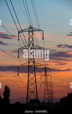 Electricity pylons at sunset silhouetted against a beautiful evening sky in English countryside. Stock Photo