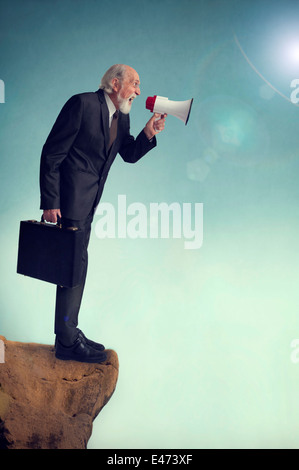 senior businessman shouting loudhailer megaphone bullhorn cliff edge Stock Photo