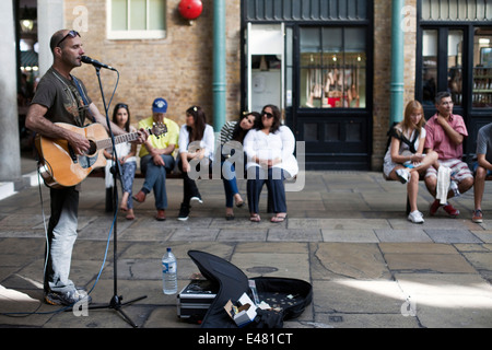 A musician sings and plays guitar to an audience in the Covent Garden Market Piazza. London, UK Stock Photo