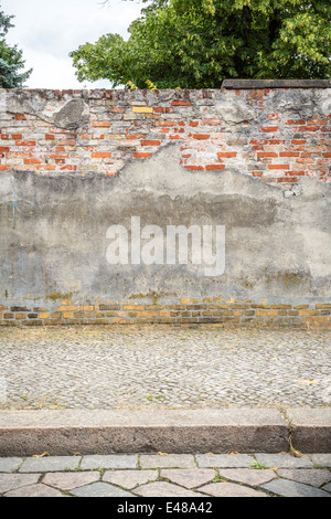old plastered red brick wall with pavement, cobblestone road and tree. Stock Photo