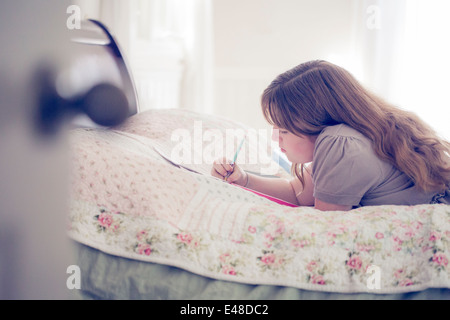 Teenage girl (13-15) lying in bed and writing Stock Photo