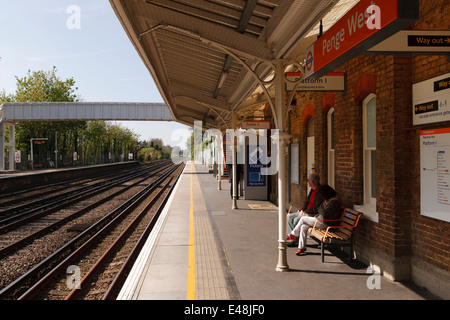 Mature couple sitting on station bench on a sunny day, waiting for a train. Stock Photo