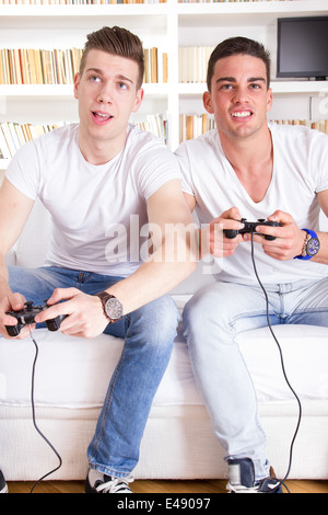 two modern guys on sofa playing computer game holding controllers Stock Photo
