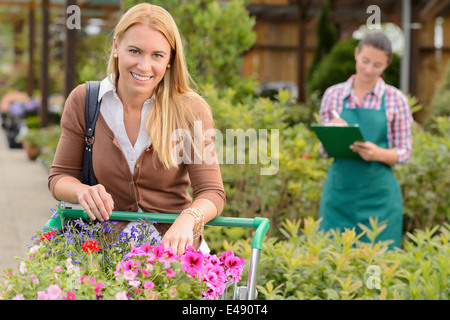 Woman shopping for flowers in garden center employee doing inventory Stock Photo