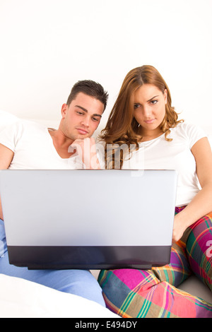 casual young happy couple enjoying using laptop computer in bed for the internet and watching movies Stock Photo