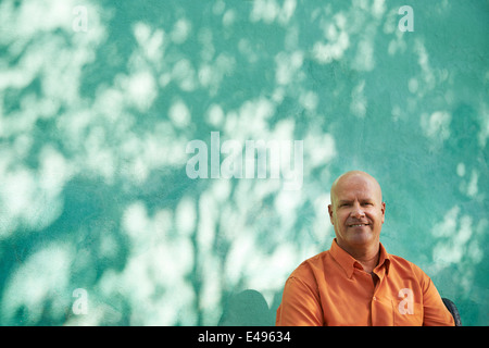 Portrait of mature caucasian man with orange shirt sitting in park and looking at camera with happy expression Stock Photo