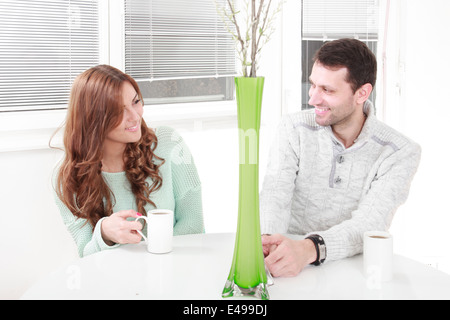 Couple relaxing together with laptop computer pc having fun. Romantic young happy couple in love sitting at home resting having fun maybe watching movie. Man and woman with cup of coffee or tea beside them on the table. Stock Photo
